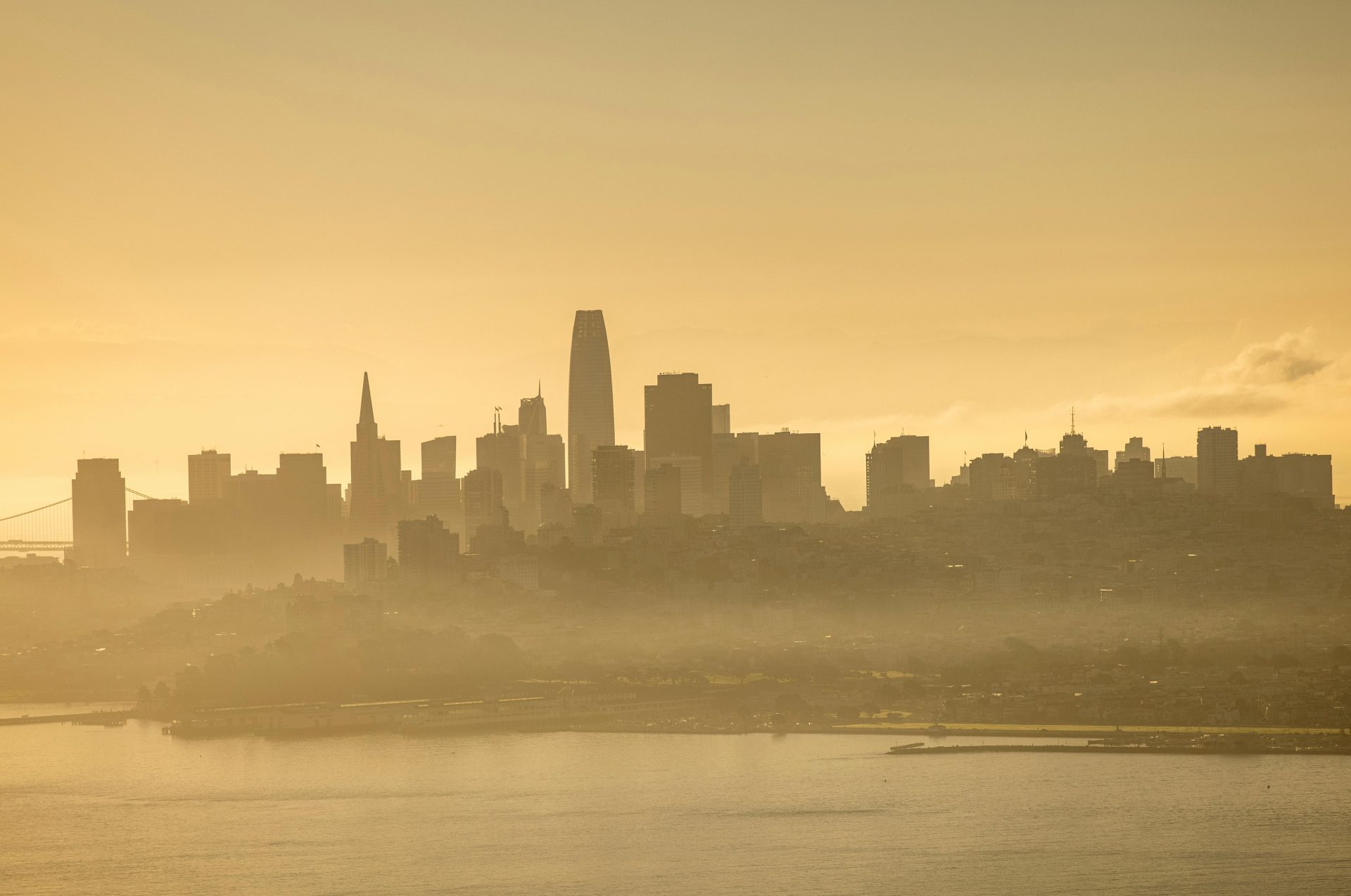 Ethereal view of San Francisco skyline at dawn with golden hues and mist.
